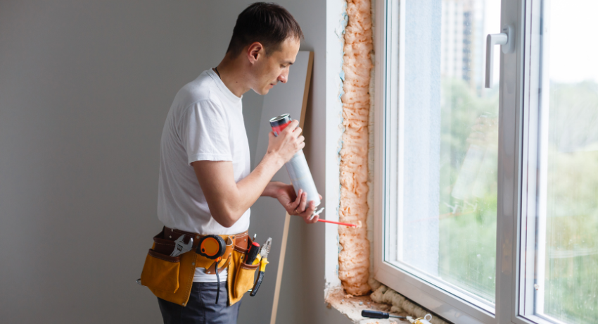 Profissional com cinto de ferramentas aplicando espuma de isolamento ao redor de uma janela.